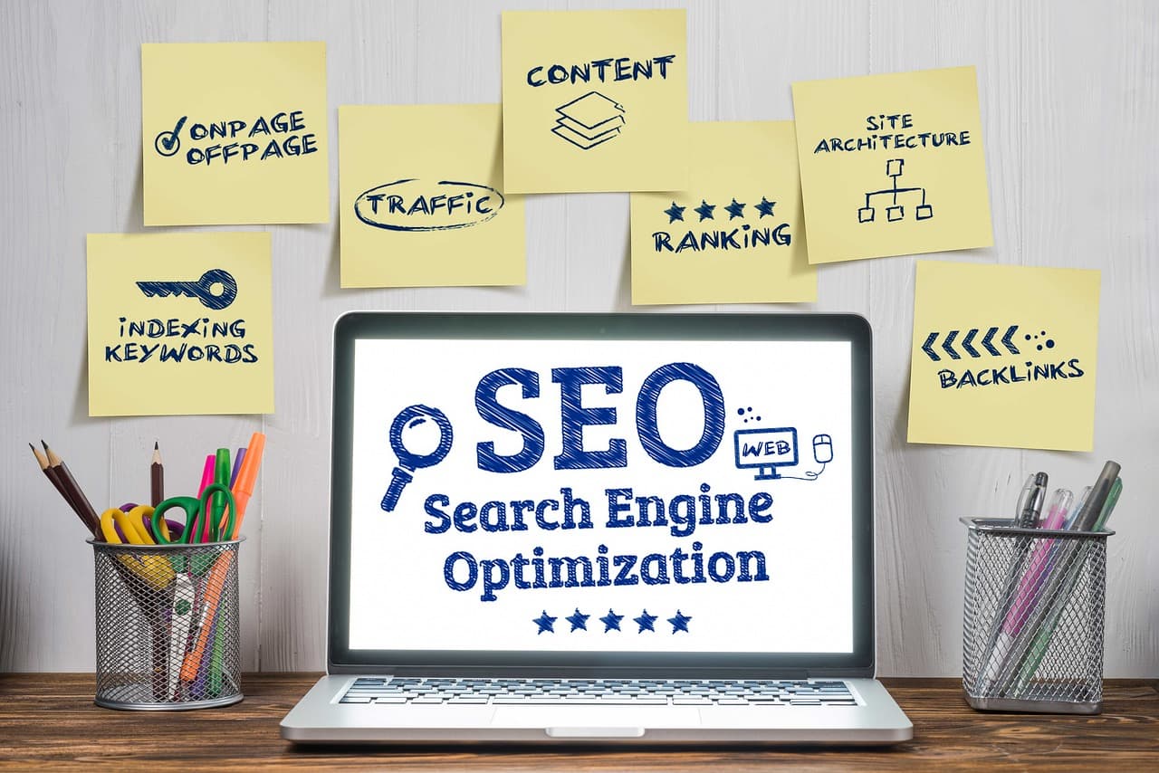 Un computer portatile che mostra la parola SEO, circondato da foglietti scritti a mano con le leve del posizionamento
