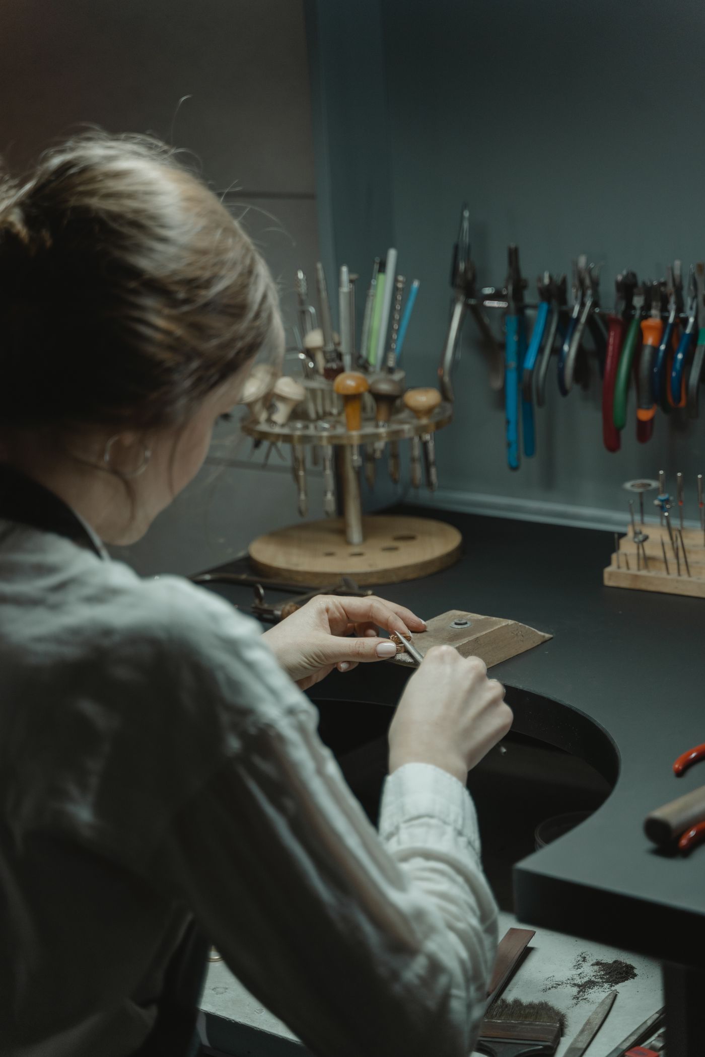 Une joaillière lime une pièce à l’établi, devant un mur d’outils